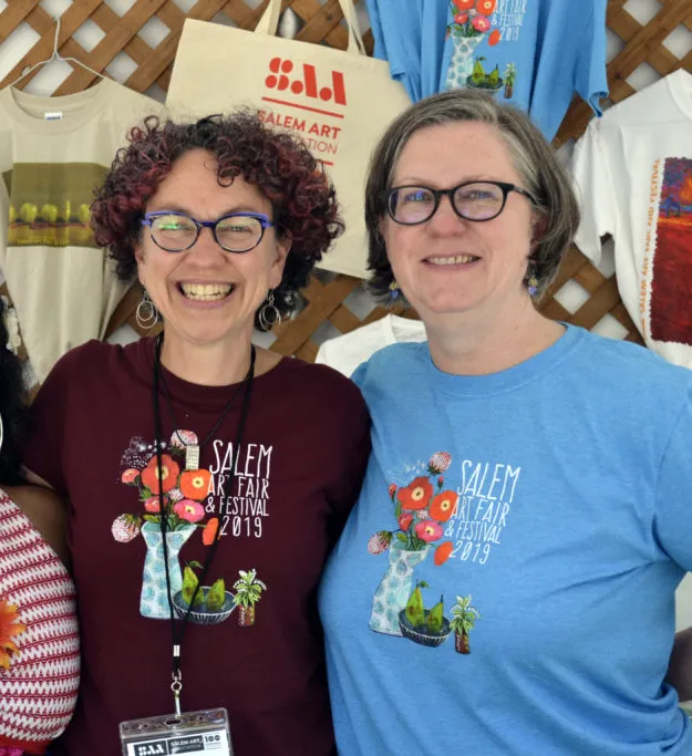 Three smiling volunteers are the festival merch booth