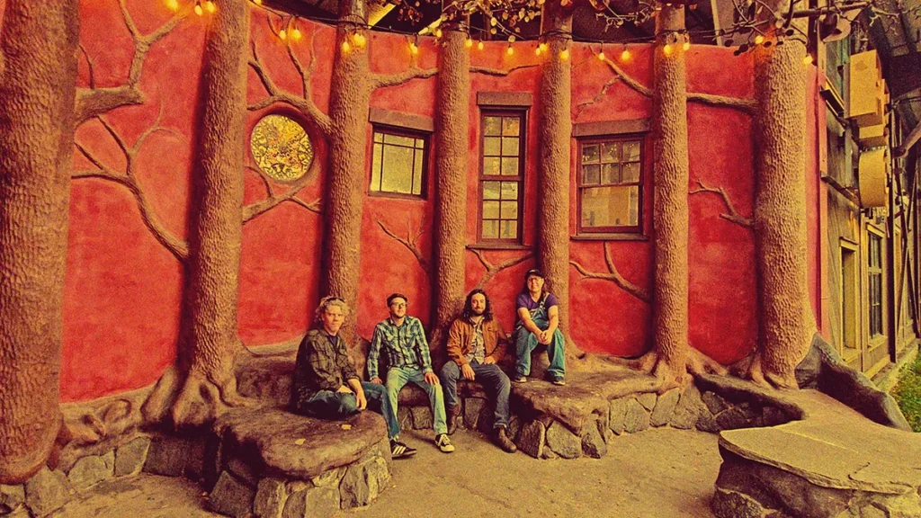 Four men sit on benches in a courtyard that are made to look like trees