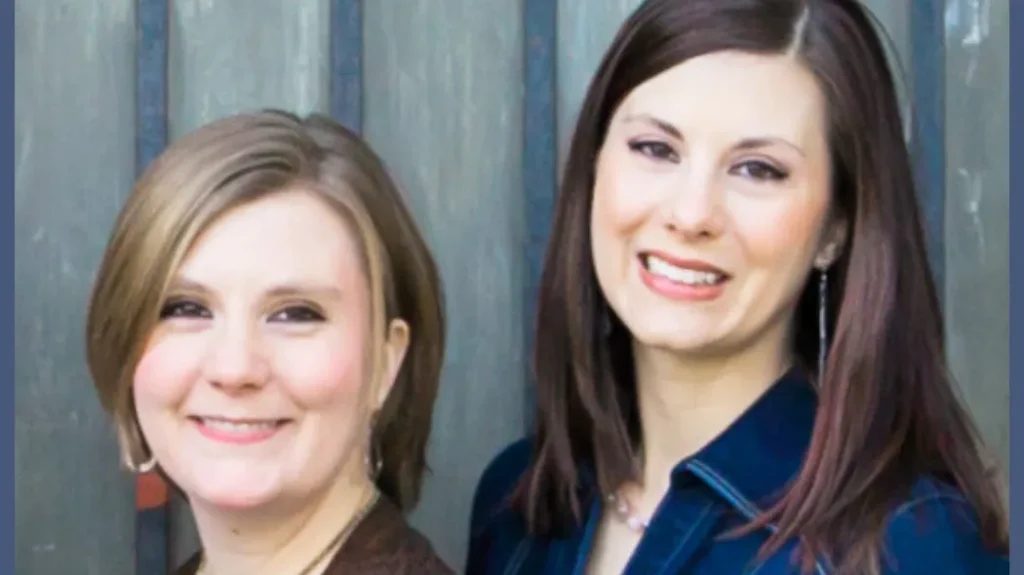 Two women, one with light brown hair and the other with dark brown hair, smile at the camera. they are standing in front of a wood backdrop.